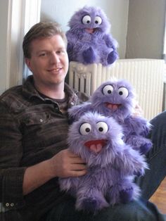 a man sitting on the floor holding three purple stuffed animals