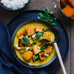 a bowl filled with curry next to bowls of rice and carrots on a wooden table