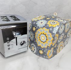 a silver toaster sitting next to a gray and yellow flowery box on a counter