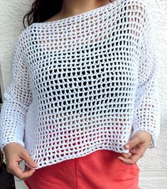 a woman is wearing a white crochet sweater and red pants with her hands in her pockets