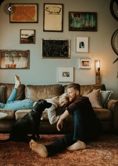 a man laying on the floor next to a black dog in front of a couch