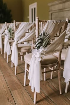 the chairs are lined up with white sashes and flowers on them, along with palm leaves