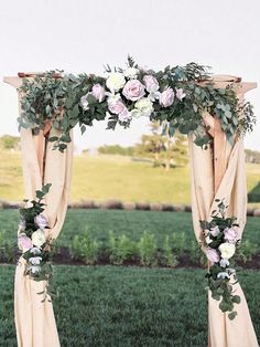 an arch decorated with flowers and greenery in front of a grassy field on a sunny day