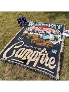 a welcome to our campfire sign is laying on the grass next to an umbrella