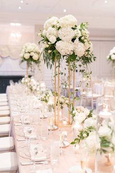 there are many tall vases filled with flowers on the long dining table at this wedding reception