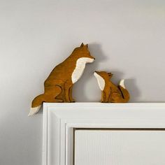 two wooden foxes sitting on top of a white door frame, one is facing the other way