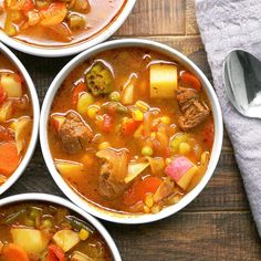 four bowls of soup with meat, vegetables and potatoes on a wooden table next to a spoon