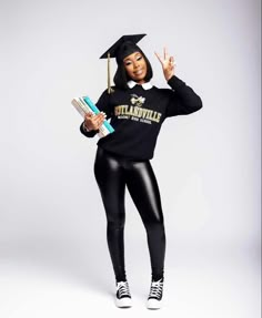 a woman in black is holding books and wearing a graduation cap with her hands up