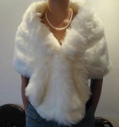 a woman is wearing a white fur vest and pearls on her necklace, standing in front of a wall