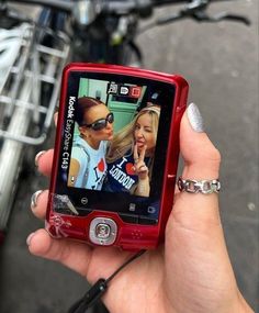 a woman holding up a red cell phone to take a picture with her friend on the screen