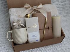 an open box containing coffee, mugs and other items on a white blanket with a gold ribbon