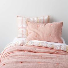 a bed with pink and white sheets and pillows on top of it, next to a wall