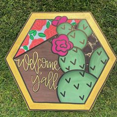 a welcome sale sign on the grass with flowers and cactuses painted on it's sides