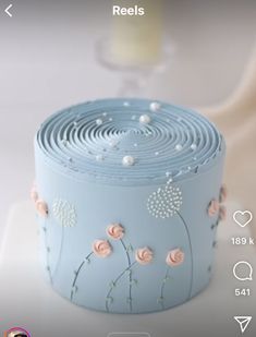 a blue cake with pink flowers on it sitting on top of a white tablecloth