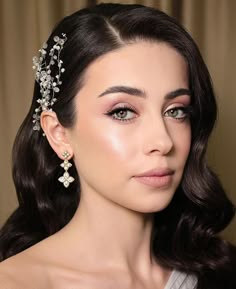 a woman with dark hair wearing a tiara and earrings on her head, looking at the camera