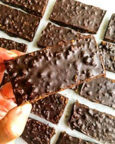 someone is holding up a chocolate brownie in front of a brick wall that has been cut into squares