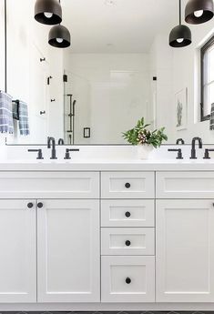 a white bathroom with two sinks and three black lights on the side of the mirror