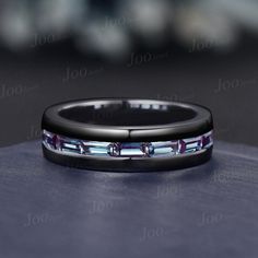 a black ring with purple and blue stones on it sitting on a table in front of a blurry background