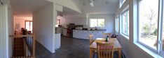 an open kitchen and dining room area in a house with white walls, wood flooring and large windows