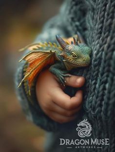 a small green and orange dragon sitting on top of a persons arm in a sweater