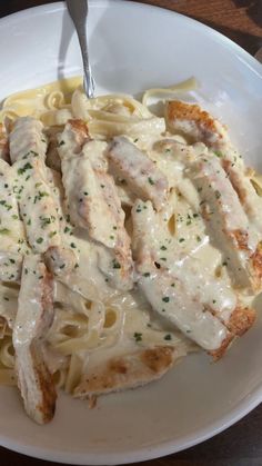 a white plate topped with pasta and chicken covered in gravy on top of a wooden table