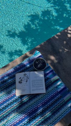 an open book sitting on top of a towel next to a pool with a bowl of water