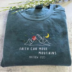 a t - shirt with the words faith can move mountains on it next to some flowers