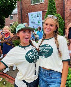 two young women standing next to each other in front of a building with people around them