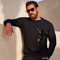 a man leaning against a wall with his hand on his hip wearing sunglasses and a black t - shirt