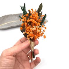 a hand holding a small bouquet of orange flowers with feathers in the backgroud