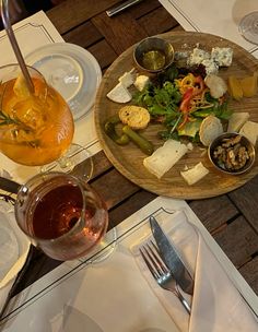 a wooden plate topped with lots of food next to glasses of wine and silverware