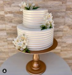 a three tiered cake with white flowers on top is sitting on a gold pedestal