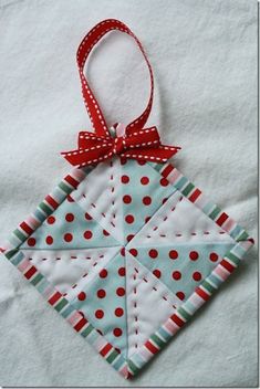 a quilted ornament hanging from a red ribbon on top of a white sheet