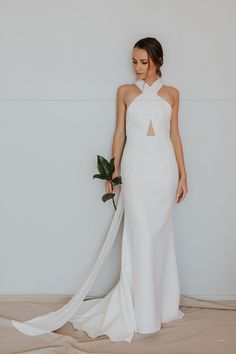 a woman in a white wedding dress holding a flower and standing next to a wall