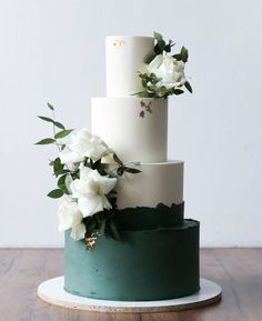 a three tiered white and green wedding cake with flowers on the top, sitting on a wooden table