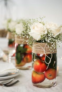 mason jar filled with apples and flowers on top of a white tablecloth covered table