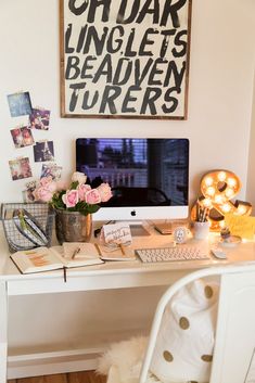 a white desk topped with a computer monitor next to a vase filled with pink flowers