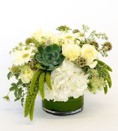 a green vase filled with white flowers and greenery