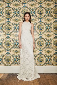 a woman standing in front of a wall wearing a white dress with an intricate pattern on it