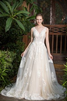 a woman in a wedding dress standing on a wooden platform with greenery behind her