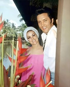 a man and woman standing next to each other in front of water with palm trees