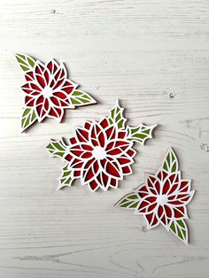 three red and green paper flowers sitting on top of a white wooden table next to each other