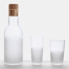 a bottle and two glasses sitting next to each other on a white surface with one empty glass in the foreground