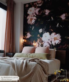 a bed sitting in front of a window next to a wall with flowers on it