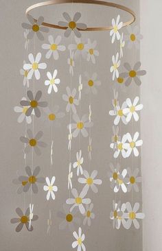 a white and yellow mobile with flowers hanging from it's center circle, in front of a gray wall