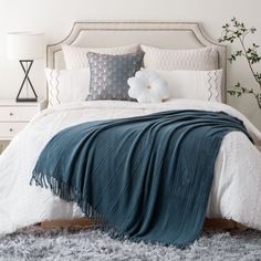 a bed with white and blue comforters, pillows and blankets on top of it