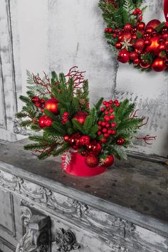 a red vase filled with christmas decorations on top of a mantle next to a wreath