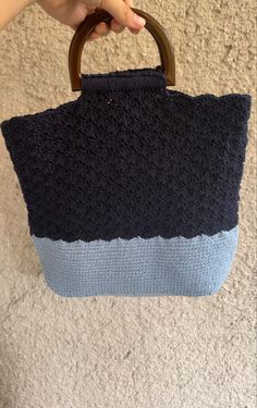 a hand holding a blue and black crocheted bag on the floor with a wooden handle