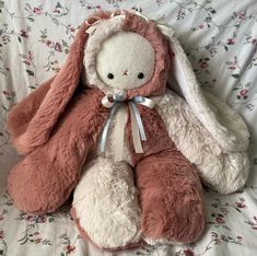 a stuffed rabbit sitting on top of a bed next to a flowered comforter