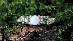 a white opal and green tourmaline ring sitting on top of a tree stump